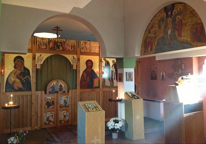 The interior of the Church is dominated by a painted wooden screen with an curtained arch in the centre. On the left of the screen is an icon of the Holy Mother in dark cloak and veiled head trimmed with gold holding the Holy Infant clhoted in gold. On the right is Christ dressed in a red robe and blue cloak, holding a gold book and raising his right hand in blessing. There story of the annunciation, the birth and childhood of Christ are depicted in icons on the panelled half-door. There are more icons along the top of the screen showing scenes from the life and death of Christ with the typical gold background of icons glowing in the light from candles in the room. On the wall to the right there is a large icon in the curved arch above an orthodox cross .